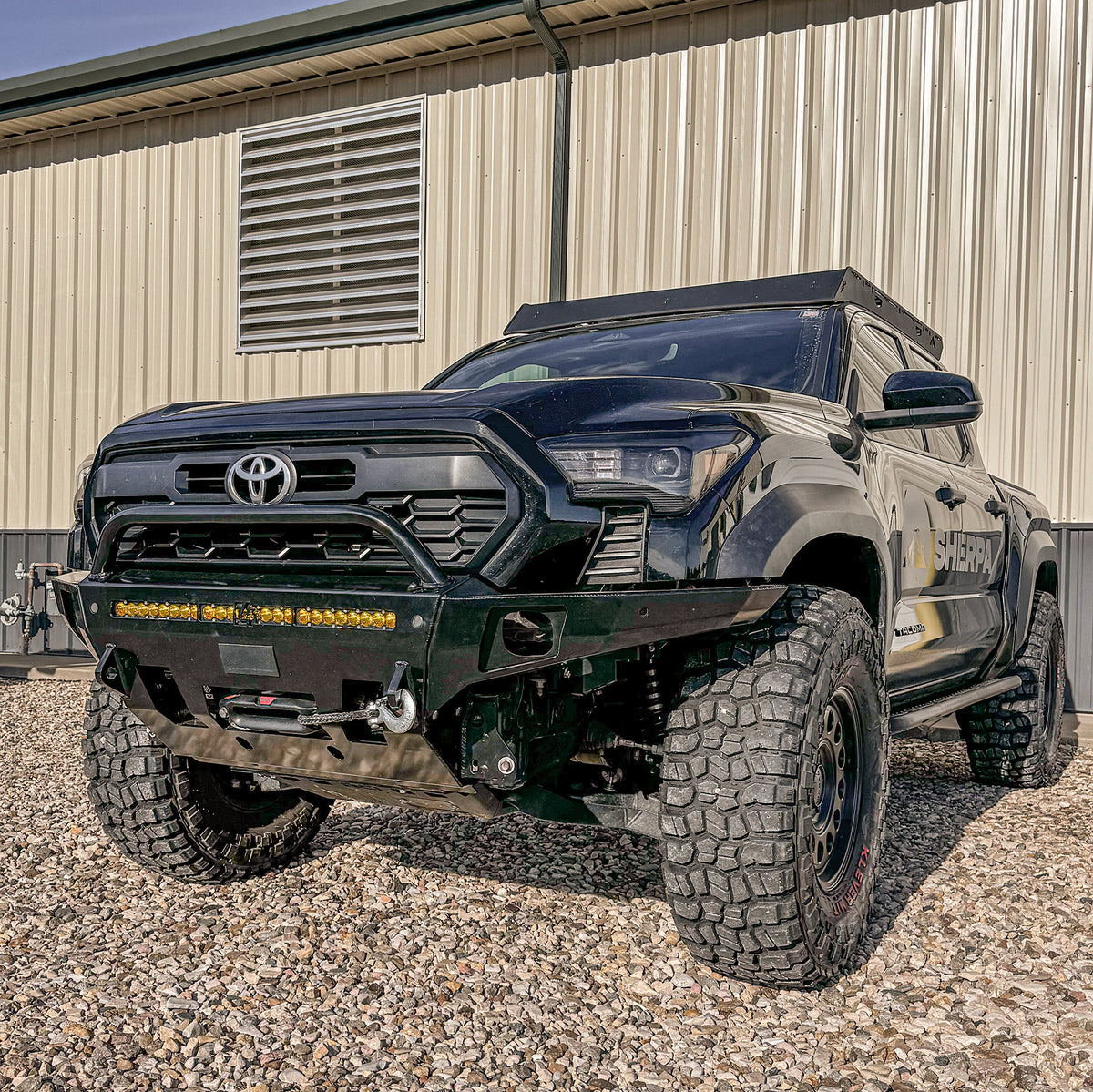 A black 2024 Tacoma sitting on gravel and showing off a freshly-installed C4 Overland bumper with low bull bar.