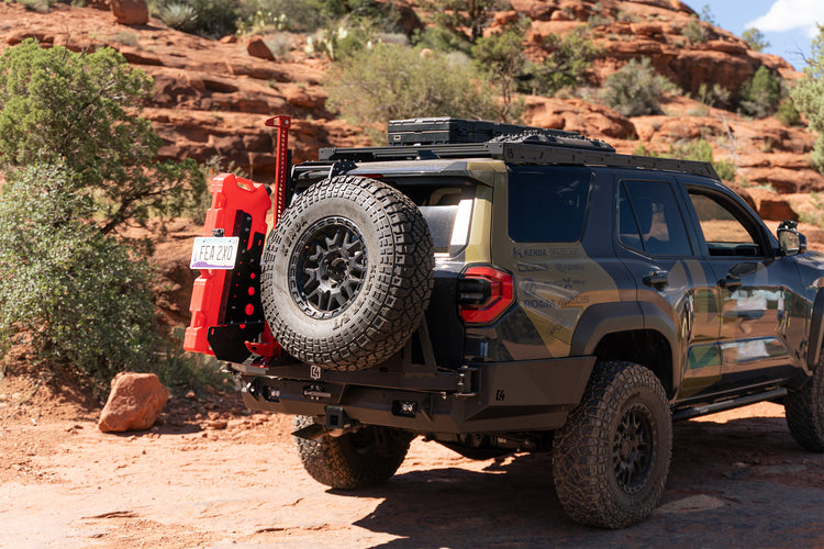A dark gray off-road 4Runner parked on a red dirt trail in Sedona, showing a C4 heavy-duty black rear bumper with swing gates holding a red fuel canister and spare tire, along with a roof rack.