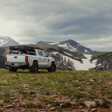 Well-equipped white Tacoma in a mountain meadow with a C4 Overland rear bumper installed.