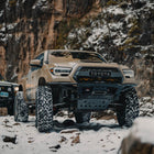 Low angle view of a tan long-travel Toyota Tacoma with the C4 minimalist Rock Runner front winch bumper installed.