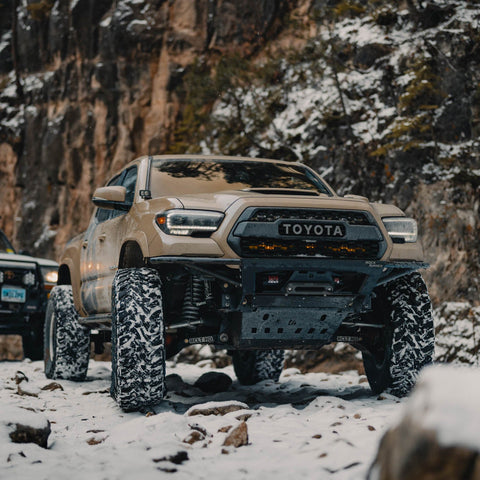 Low angle view of a tan long-travel Toyota Tacoma with the C4 minimalist Rock Runner front winch bumper installed.