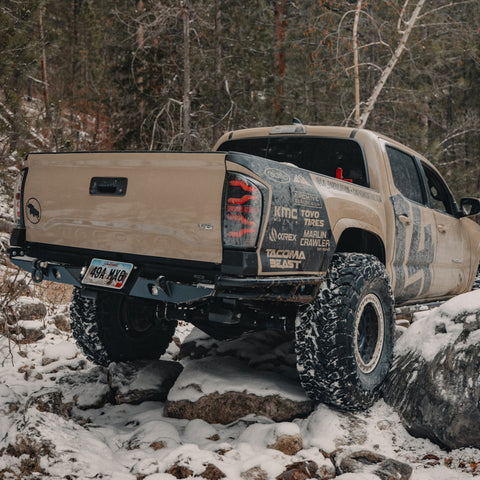 Tan Tacoma rock crawling in the snow and showing off the C4 Rock Runner rear bumper and its extreme departure angle.