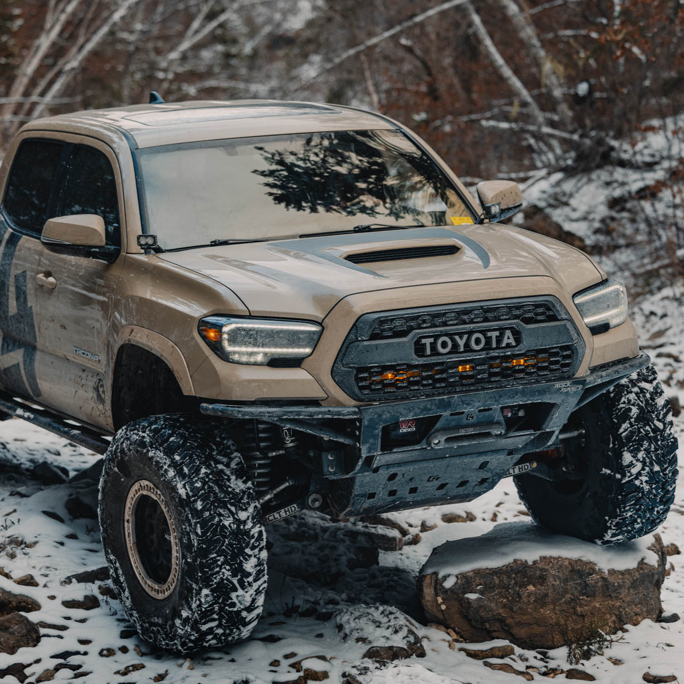 Tan C4 shop Tacoma offroading in the snow with a Rock Runner front winch bumper installed.