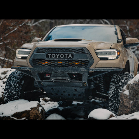 Front view of the C4 Rock Runner bumper for the 3rd Gen Tacoma deep in a rock garden while wheeling in the snow.