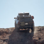 The C4 4Runner build summits a steep rock crawl, equipped with bumpers, roof rack, ladder, and MOLLE panels.