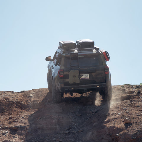 The C4 4Runner build summits a steep rock crawl, equipped with bumpers, roof rack, ladder, and MOLLE panels.