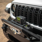 Close-up of a Jeep front bumper with DV8 Xtract 12k Synthetic Rope Winch on a blurred natural background