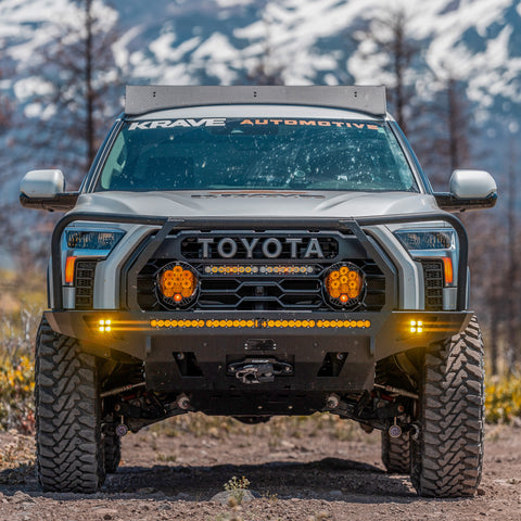 White Toyota Tundra on a dirt road with snow-capped mountains in the background and a C4 Overland front bumper prominently featured on its front end.
