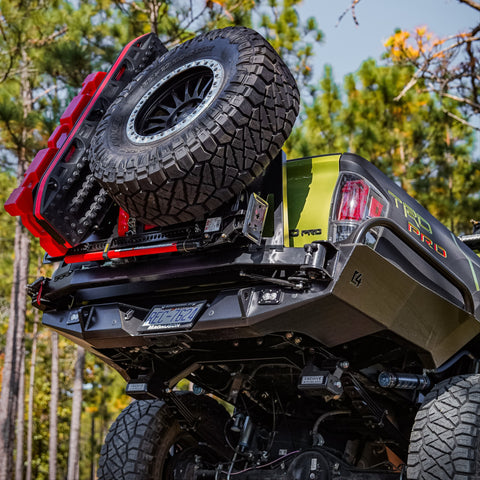 Tacoma sticking its tail in the air crossing an obstacle in the mountains, shwoing off the steel structure of the C4 Overland High Clearance rear bumper with spare tire swing-out and accessory mounts installed. 