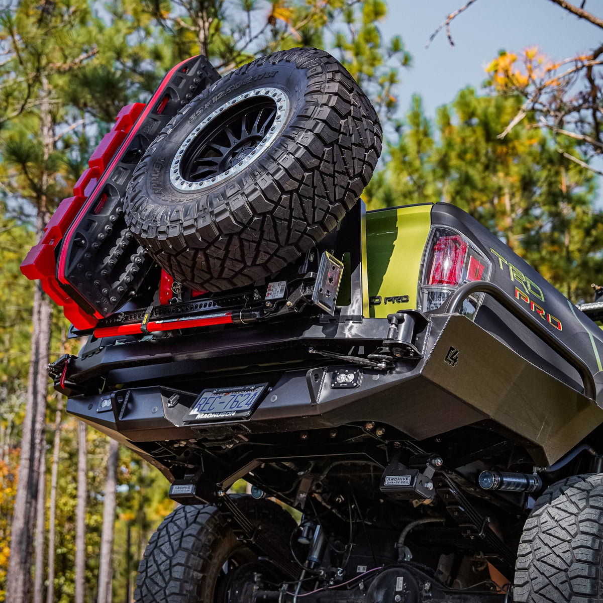 Tacoma sticking its tail in the air crossing an obstacle in the mountains, shwoing off the steel structure of the C4 Overland High Clearance rear bumper with spare tire swing-out and accessory mounts installed.