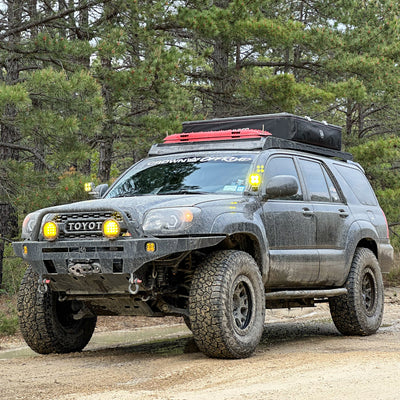 Black 4th Generation 4Runner on a muddy mountain road fully equipped for overland travel to include a lift and oversized tires, a roof rack with MaxTrax, a rooftop tent, auxiliary lighting, winch and a steel bumper from C4 Fabrications.