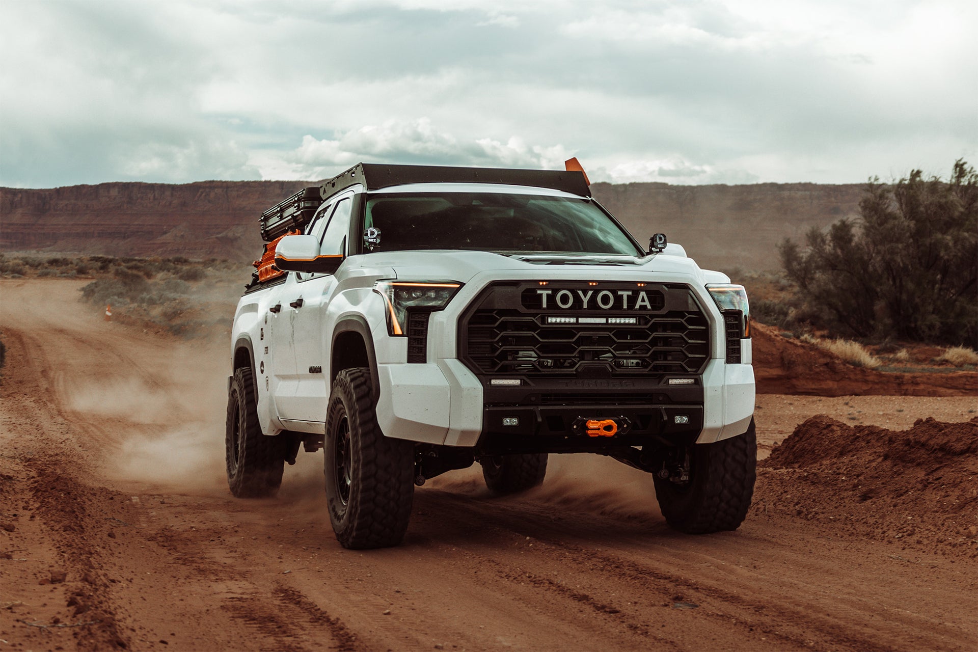White Toyota Tundra driving on a dirt road with a desert landscape in the background.