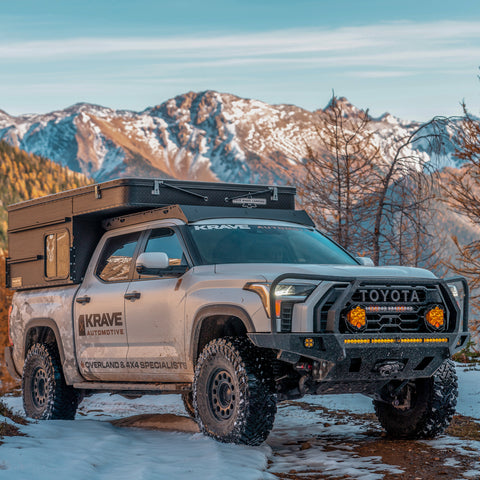 White CrewMax Tundra parked in the mountains with overland bumper and Four Wheel Camper.