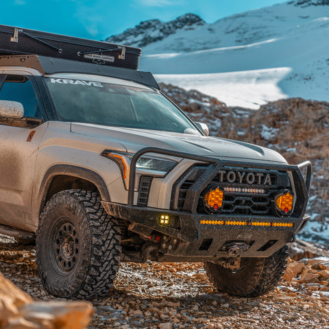 Close-up quartering view of the C4 Overland bumper for the 3rd Generation Toyota Tundra with lighting installed and the full-height bull bar option with headlight hoops. 