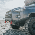 Low-angle view of the C4 High Clearance Additions and Lo-Pro bumper for the 4Runner on a beach with people walking the surf in the background.