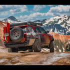 Maroon 4Runner offroading in the mountains with a rear tire fully stuffed into the wheelwell, showing off the C4 Fabrications rear bumper with full-width single swing-out tire carrier.