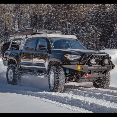 Black Tacoma spinning tires in the snow and equipped with a C4 Overland front bumper.