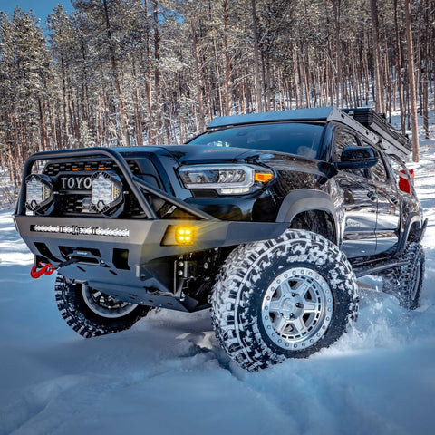Black 3rd Gen Tacoma stanced up in the snow and equipped with a C4 Overland bumper with full-height bull bar and tube gussets.
