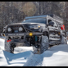 Black four-door Tacoma wheeling in the snow with an Overland winch bumper.