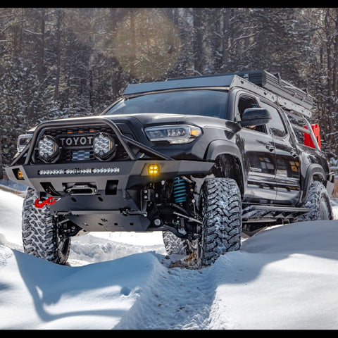 Black four-door Tacoma wheeling in the snow with an Overland winch bumper.