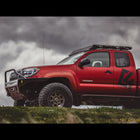 Low-angle side view from a distance of a red extended cab 2nd Generation Tacoma with the C4 Overland winch bumper installed.