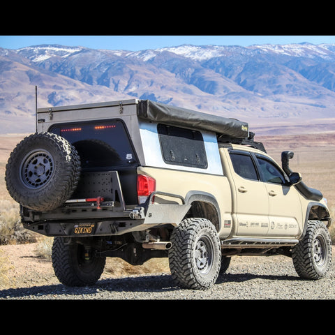 Tan Tacoma with full overland accessories sitting in a desert valley with mountains in the background. 