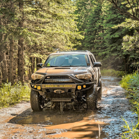 Action photo of a 2014+ 4Runner splashing through a wet and muddy mountain trail and equipped with a C4 Hybrid winch bumper.
