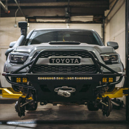 Tacoma on lift with the wheels off and equipped with a Hybrid bumper from C4 Fabrication.
