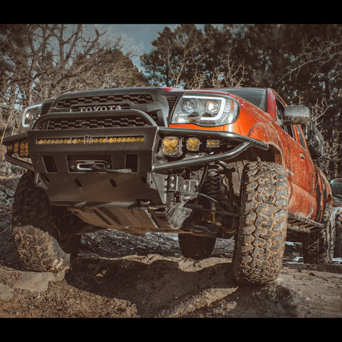 Red 2nd Gen Tacoma wheeling in teh mountains and climbing up over a rock feature, the C4 Hybrid bumper leading the way.