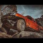 Low angle shot of a red Tacoma climbing rocks with a C4 Fabrication winch bumper.